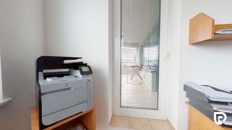 Printer on a wooden shelf, next to glass doors with vertical blinds.