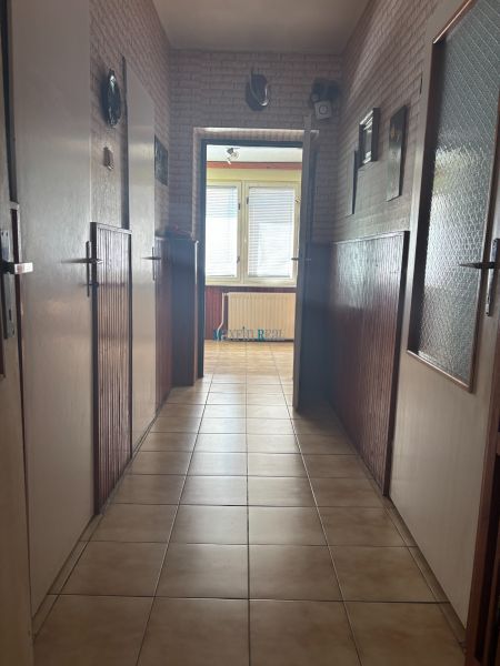 A hallway in a family house with tiles, lined with walls, leading to windows with blinds.