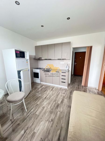 A kitchenette in a studio apartment with a wood-patterned floor, kitchen cabinets, and appliances.