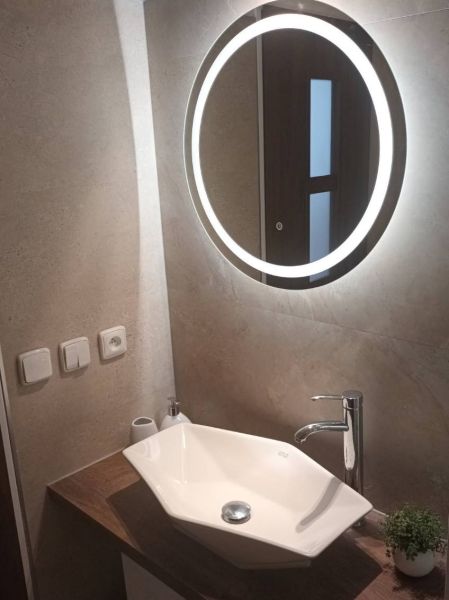 A bathroom with a mirror with LED lighting and a modern sink in a studio apartment.