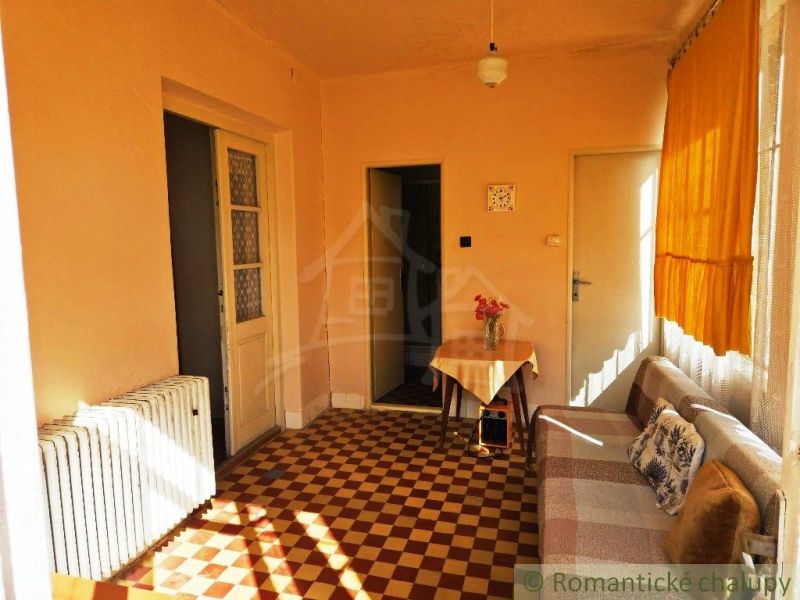 Interior of a family house with a sofa, table, radiator, and checkered floor.