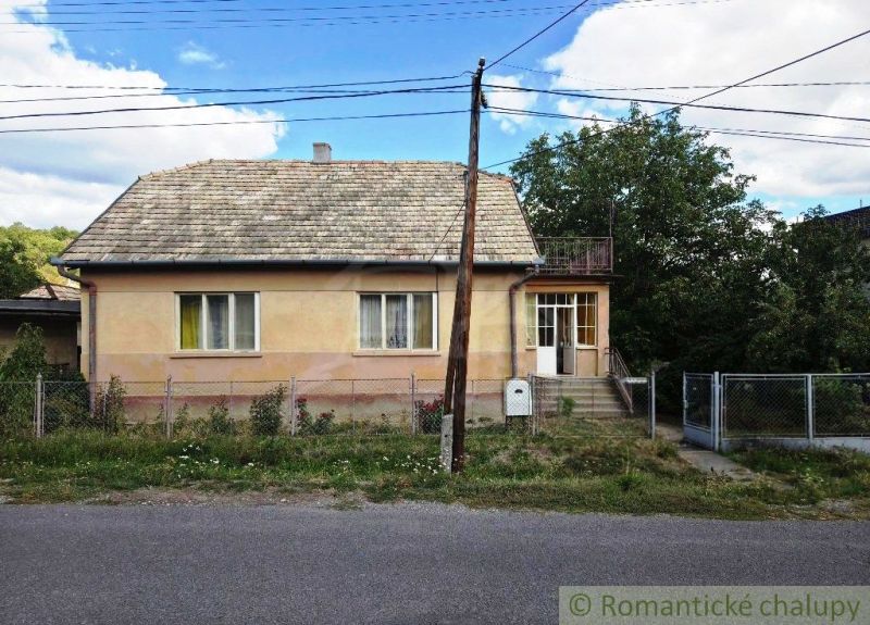 A family house in Sečianky with a garden, fence, and veranda on a sunny street.