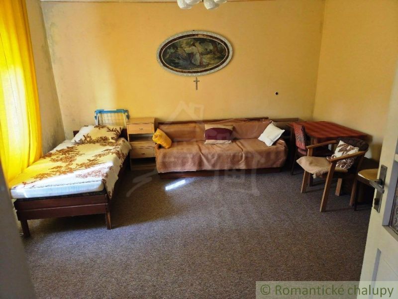 A room in a family house with a sofa, bed, and chairs in warm colors.