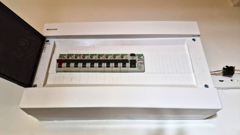 An electrical distribution box in a studio apartment with plug-in circuit breakers and an open cover.