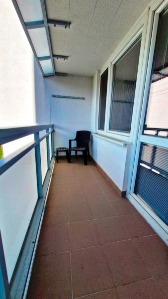 A balcony in a studio apartment with a plastic chair and tiles on the floor.