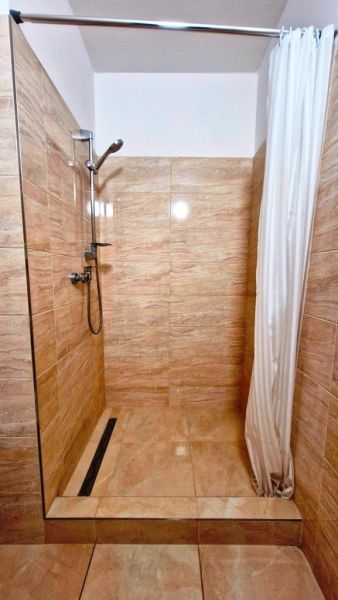 A shower corner with beige tiles in a studio apartment.