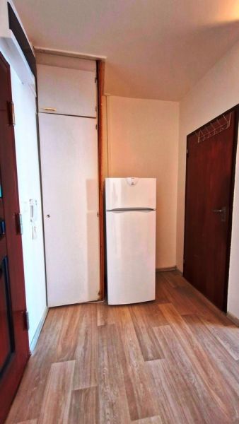 A refrigerator with a wooden floor decor and white cabinets in a studio apartment.