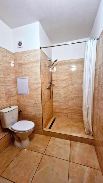 Studio apartment bathroom with a toilet and a shower, tiled with ceramic tiles.