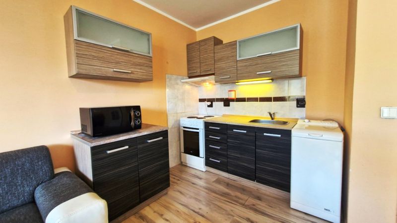A kitchenette in a studio apartment with a microwave, a cooktop, and a wooden decor floor.