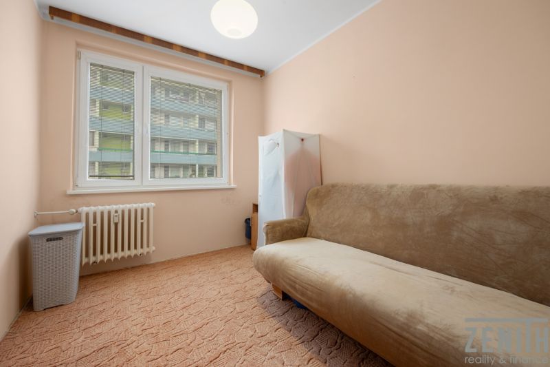 A room with a beige sofa in a 4-room apartment, a carpet, and a radiator.