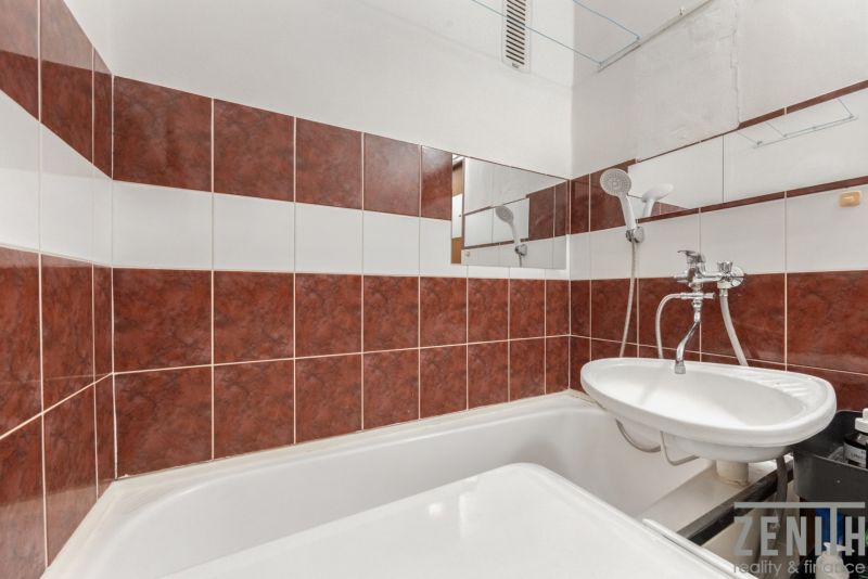 Bathroom in a 4-room apartment with a bathtub and a sink, dark tiles.