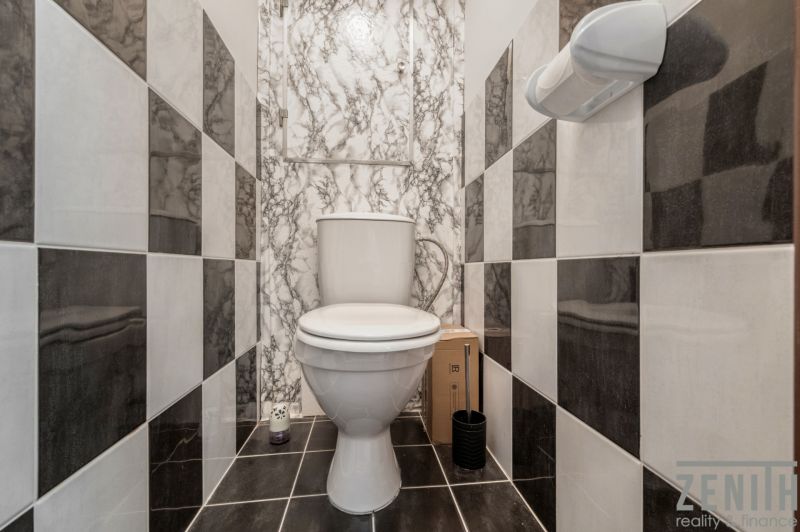 A toilet with black and white wall tiles in a 4-room apartment.