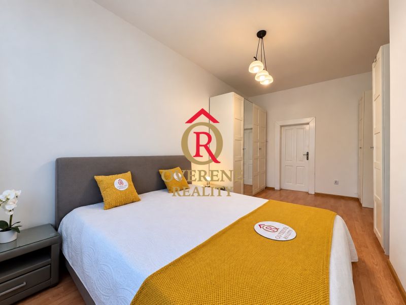 Bedroom in a two-room apartment with a wooden decor floor and white furniture.