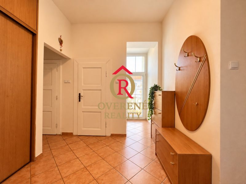 Entrance hallway of a 2-room apartment with tiles and wooden furniture, light streaming through a tall window.