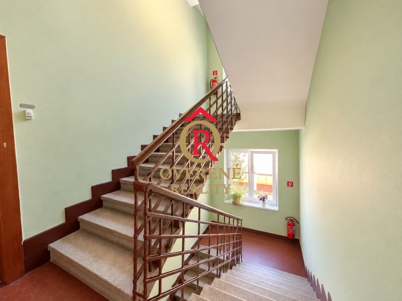 A staircase in a 2-room apartment with a room window, light-colored walls, and a fire extinguisher.