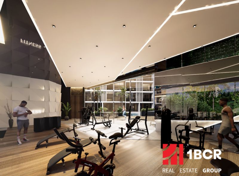 The interior of a gym with wood-patterned flooring and exercise machines. Apartment construction.