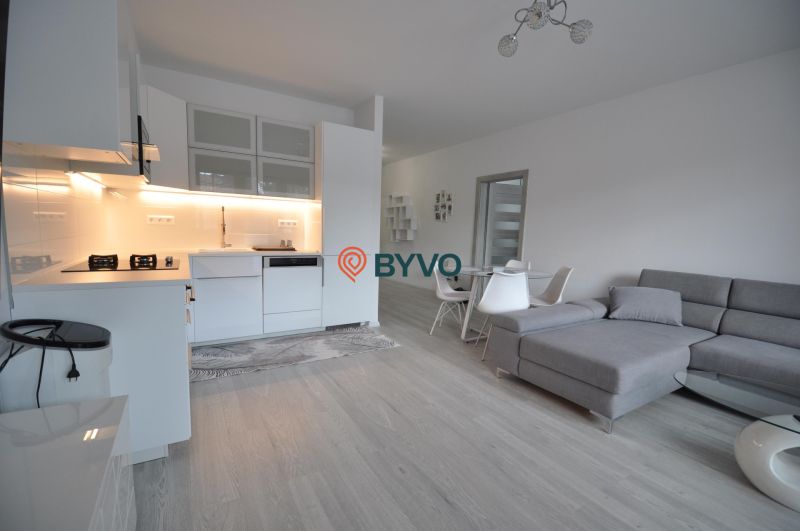 A bright kitchen with a sofa and a dining table, a two-room apartment with a wood-patterned floor.