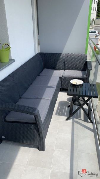 A balcony in a 2-room apartment with a rattan sofa and a small table.