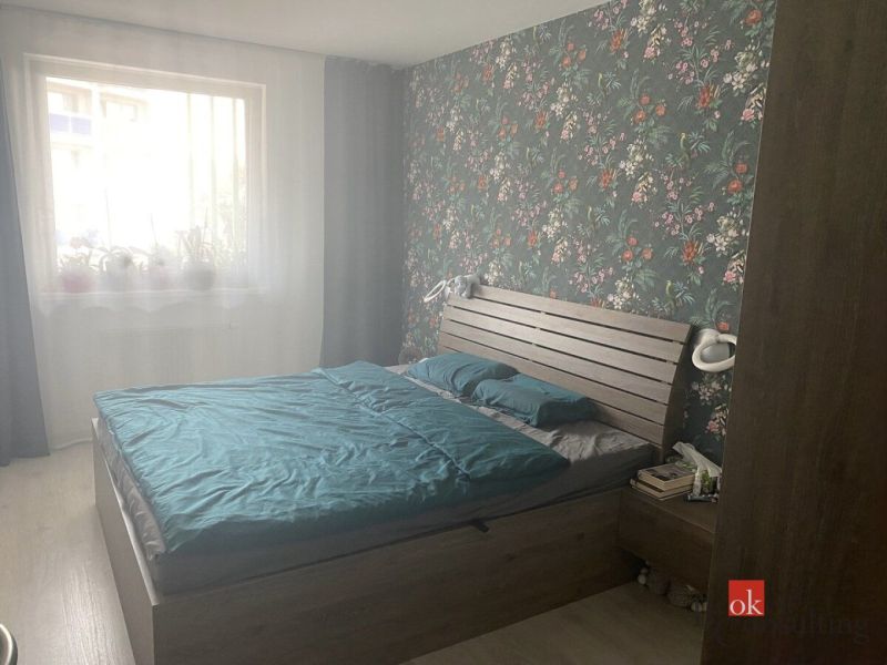 Bedroom in a two-room apartment with floral wallpaper and wooden decor flooring.