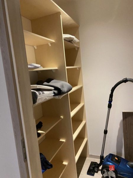 A storage unit with shelves, in the corner of the room, next to a vacuum cleaner.