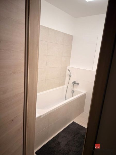 A bathroom with a bathtub and beige tiles in a 2-room apartment.
