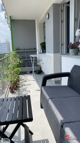 A balcony of a 2-room apartment with comfortable seating, a table, and plants.