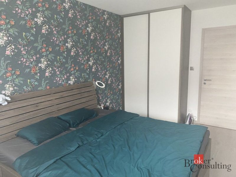 A bedroom with floral wallpaper, a double bed, a wardrobe, and composite flooring.