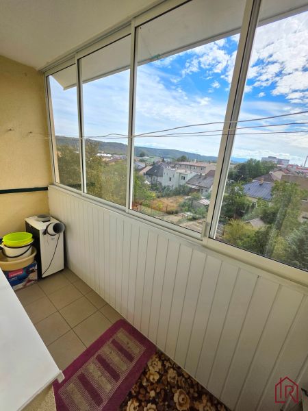 Glazed loggia with a view of the rooftops and greenery in a 2-room apartment.