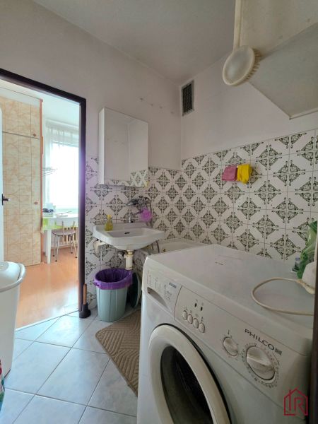 Bathroom in a 2-room apartment with a washing machine, white tiles, and a sink.