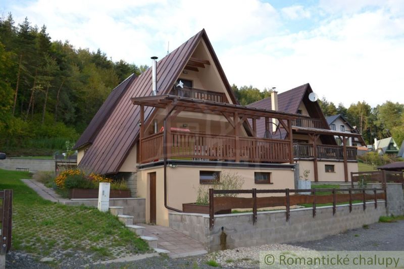 A cottage in Nižná Polianka with wooden details, surrounded by greenery and forest.