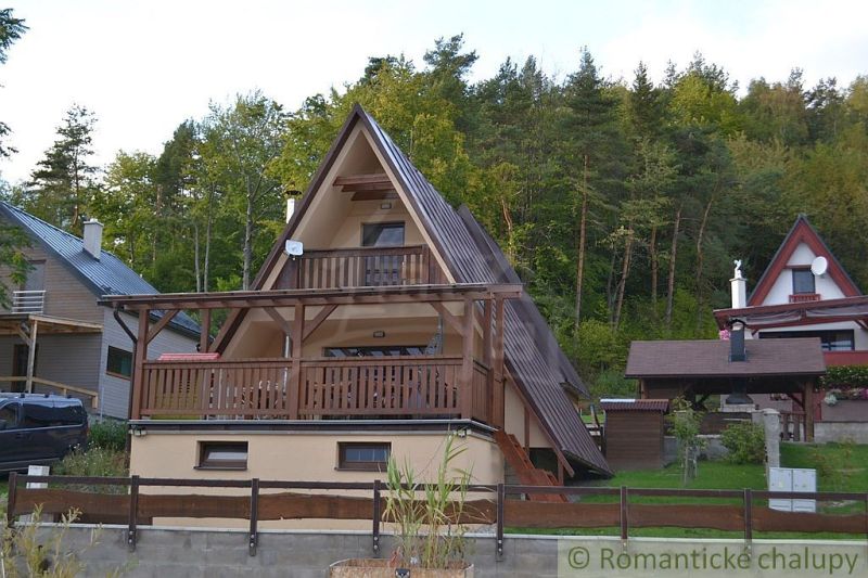 A wooden cabin in Nižná Polianka surrounded by forest, with a wooden balcony and terrace.