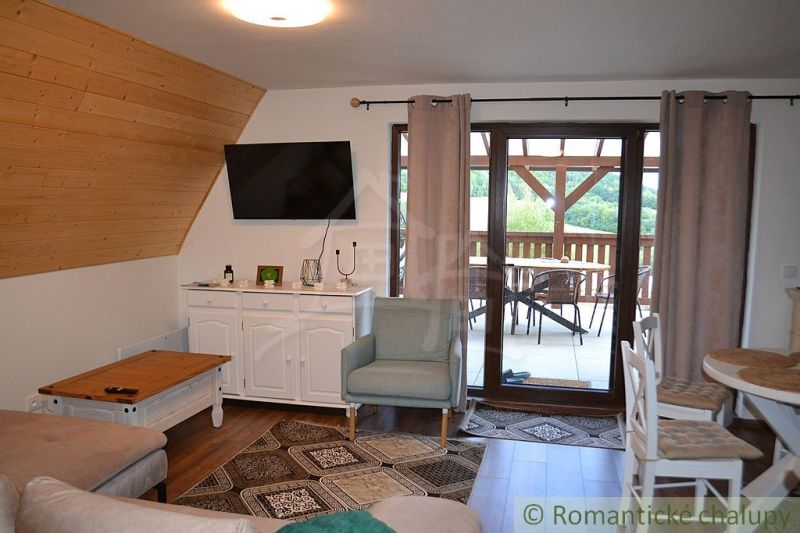 A cottage with a living room, wooden decor flooring, and a view of the terrace with seating.