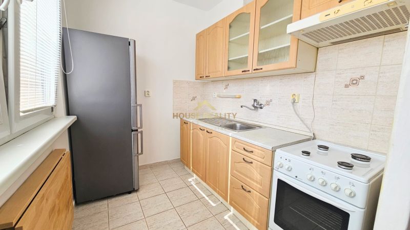 A kitchen in a studio apartment with a refrigerator, stove, and light-colored furniture.