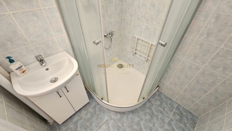Bathroom with a sink, shower stall, and tiles in a studio apartment.