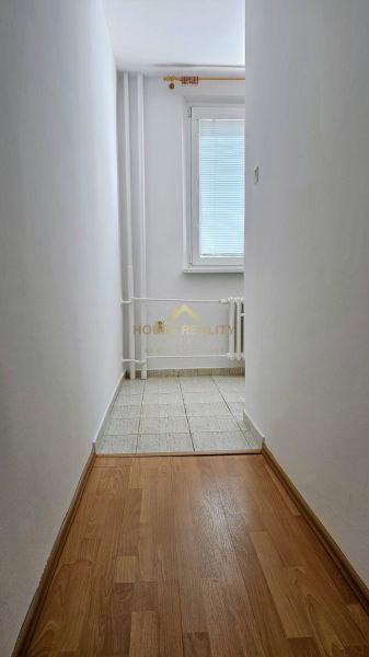 A narrow corridor with white walls, a window, and a floor with a wooden decor.