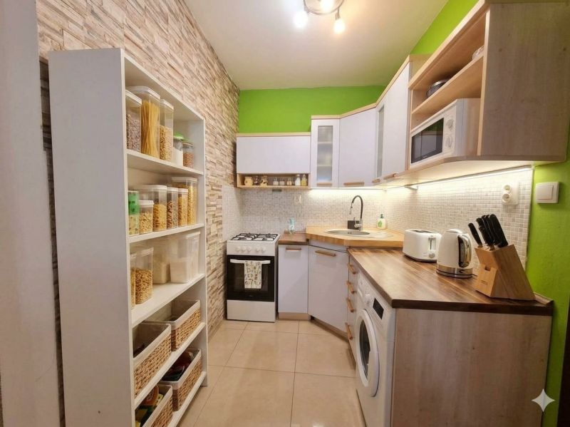 A kitchen in a 2-room apartment with shelves, appliances, and wooden decor on the countertop.