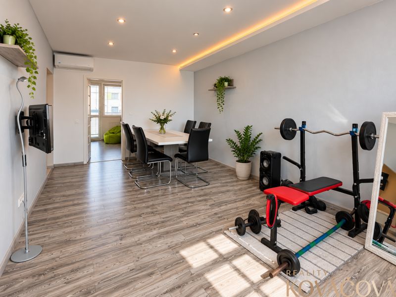 Dining room in a 4-room apartment with a table, a workout bench, and a wooden-patterned floor.