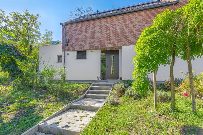 A family house in Vtáčie údolie, Bratislava - Koliba, surrounded by greenery and a paved walkway.