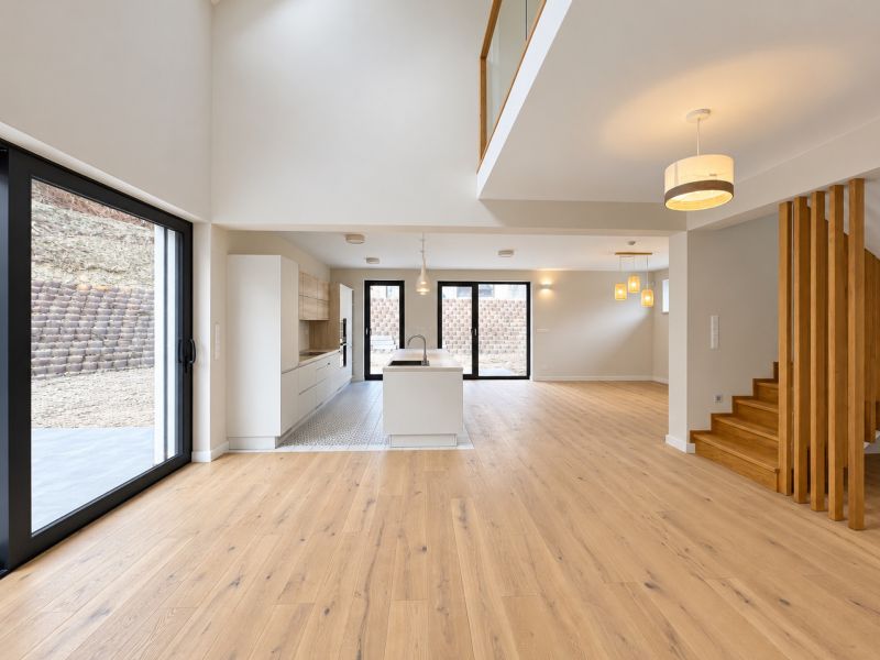 Open space in a family house with a kitchen, large windows, and wooden decor flooring.