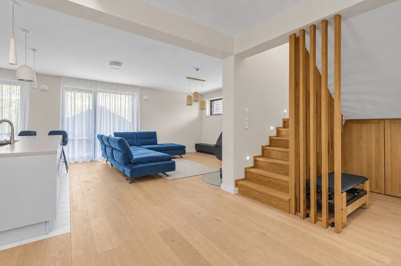 Interior of a family house with a blue sofa, wooden decor flooring, and a staircase.