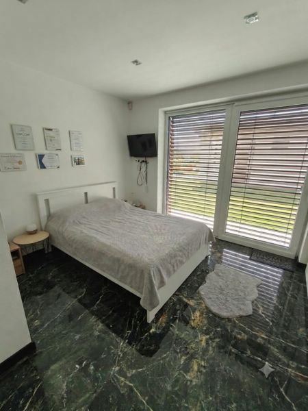 A bedroom in a family house with a bed and a television, marble floor, large window.