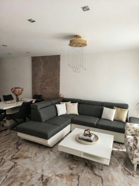 Living room in a family house with a corner sofa, modern table, and stylish chandelier.