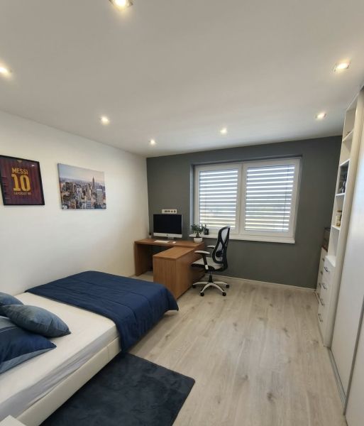A room in a family house with a computer desk, a bed, and a wooden decor floor.