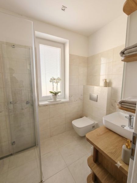 A bathroom in a family house with soft beige tiles, an elegant sink, and a shower enclosure.