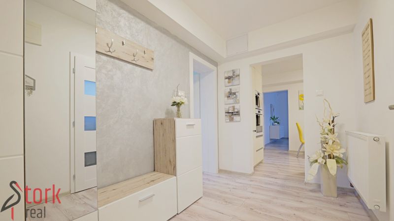 Entrance hallway of a 4-room apartment with a wooden decor floor and white furniture.