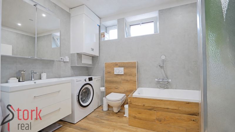 Bathroom in a 4-room apartment with wood-patterned flooring, a washing machine, and a bathtub.