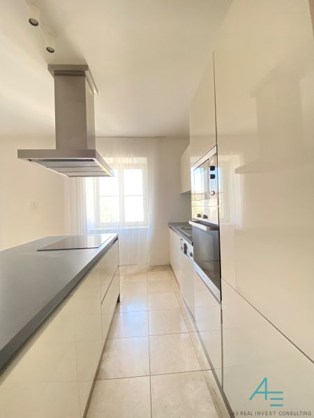 A kitchen in a 3-room apartment with glossy cabinets and a range hood by the window.