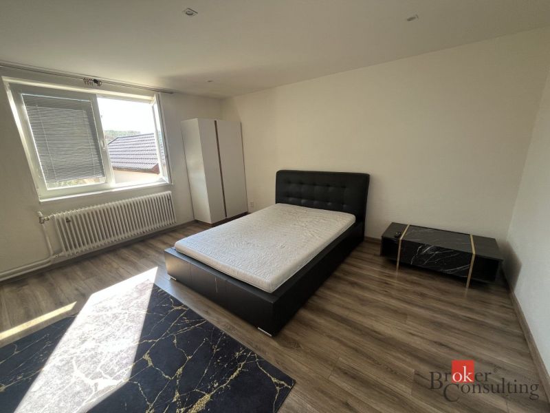 A bedroom with light from a window, a bed, a wardrobe, and a floor with a wooden decor.