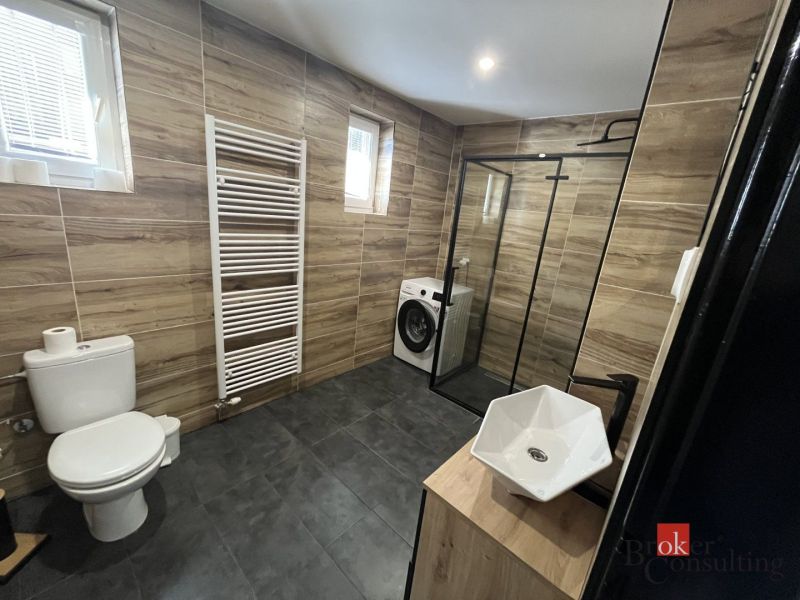 Bathroom in a 4-room apartment with a sink, shower, and washing machine, floor with wooden decor.