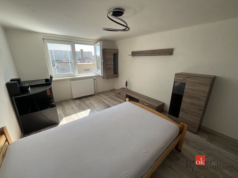 A bedroom in a 4-room apartment with a wooden decor floor, simple furniture, and a large window.